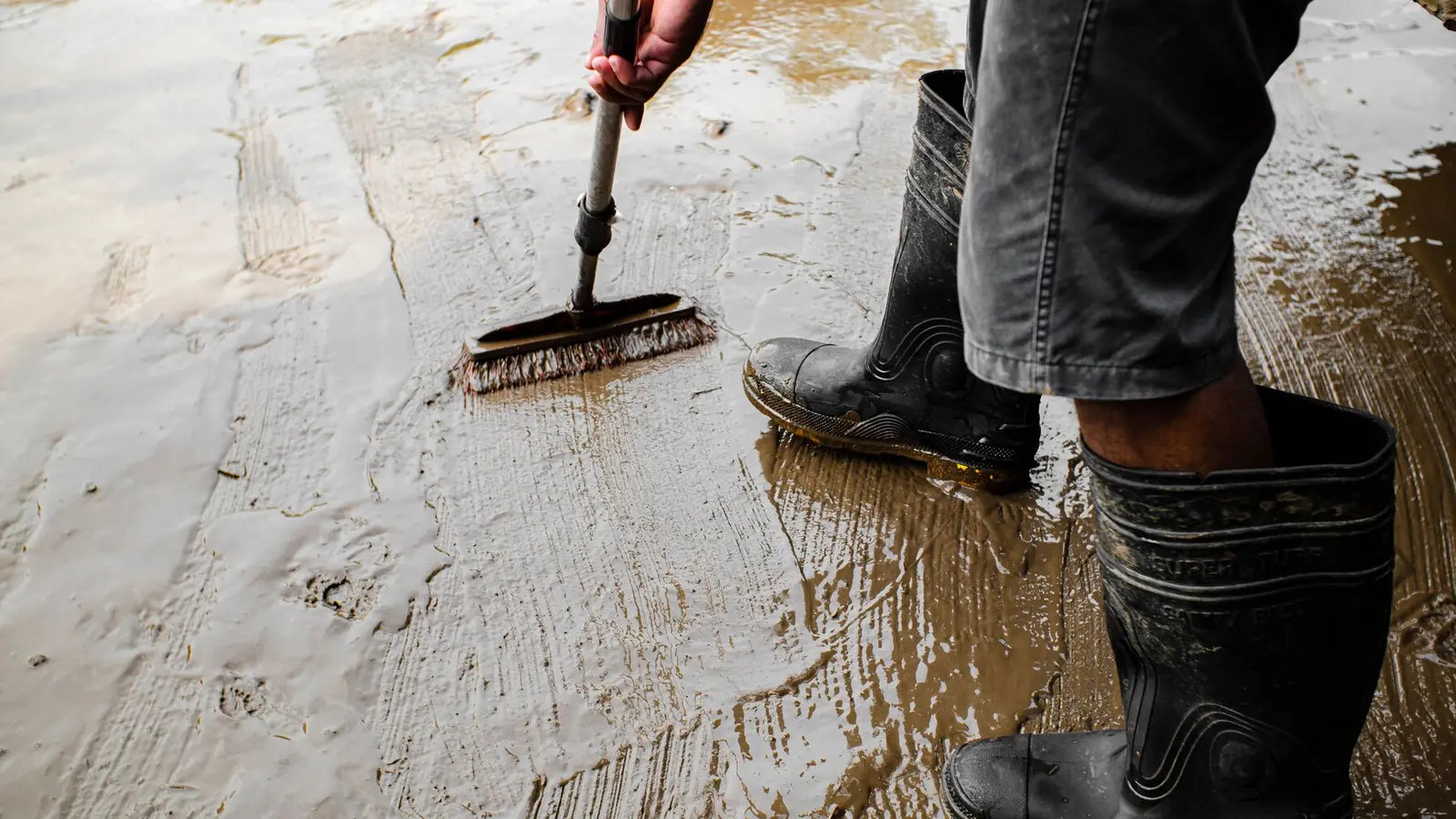 Gruntowanie betonowej wylewki szczotką na kiju, z widoczną granicą mokrej i suchej powierzchni