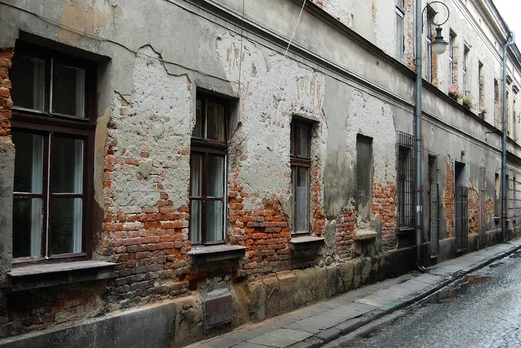 Nieodnowiona kamienica przy brukowanej uliczce, z tynkiem odpadającym od ceglanego muru